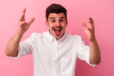 Pembe arka planda izole edilmiş genç beyaz adam hoş bir sürpriz alıyor, heyecanlı ve el kaldırıyor..