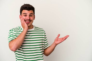 Beyaz arka planda izole edilmiş genç beyaz bir adam bir avuç içinde fotokopi alanı tutuyor, el üstünde tutuyor. Şaşırmış ve mutlu..