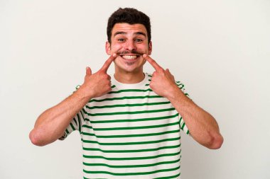 Beyaz arka planda izole edilmiş genç beyaz adam gülümsüyor, parmaklarını ağıza doğrultuyor..