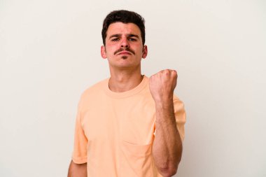 Beyaz arka planda izole edilmiş genç beyaz bir adam yumruğunu kameraya gösteriyor, agresif bir yüz ifadesi..