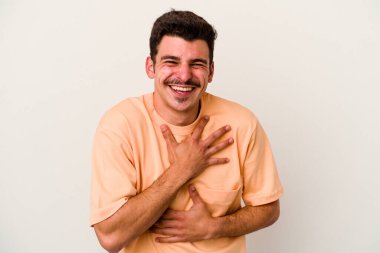 Beyaz arka planda izole genç beyaz adam mutlu bir şekilde gülüyor ve ellerini karnının üstünde tutarak eğleniyor..