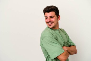 Beyaz arka planda izole edilmiş genç beyaz adam kollarını kavuşturarak gülümsüyor..