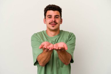 Beyaz arka planda izole edilmiş genç beyaz bir adam elinde avuç içi bir şeyle kameraya sunuyor..