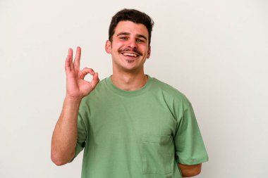 Beyaz arka planda izole edilmiş genç beyaz bir adam bir göz kırptı ve elleriyle iyi bir jest yaptı..