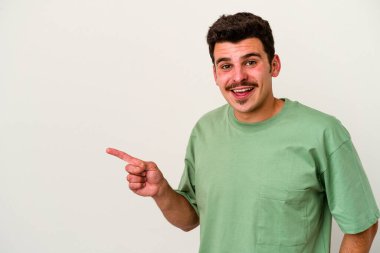 Beyaz arka planda izole edilmiş genç beyaz adam işaret parmağıyla işaret ederek gülümsüyor..
