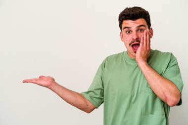 Beyaz arka planda izole edilmiş genç beyaz adam, avuç içi fotokopi alanını elinde tutmaktan etkilenmiş..