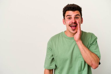 Beyaz arka planda izole genç beyaz adam yüksek sesle bağırıyor, gözleri açık ve elleri gergin tutuyor..