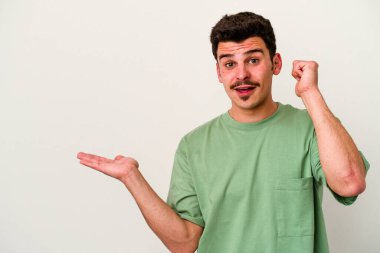 Beyaz arka planda izole edilmiş genç beyaz bir adam bir avuç içinde fotokopi alanı tutuyor, el üstünde tutuyor. Şaşırmış ve mutlu..