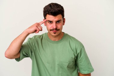 Beyaz arka planda izole edilmiş genç beyaz bir adam şakağı parmağıyla işaret ediyor, düşünüyor ve bir göreve odaklanıyor..