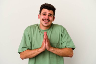 Beyaz arka planda izole edilmiş genç beyaz bir adam el ele tutuşup, ağız kenarında dua ediyor, kendinden emin..