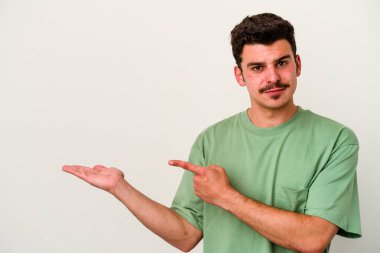 Beyaz arka planda izole edilmiş genç beyaz bir adam, palmiye üzerinde bir fotokopi alanı tutarken heyecanlı..