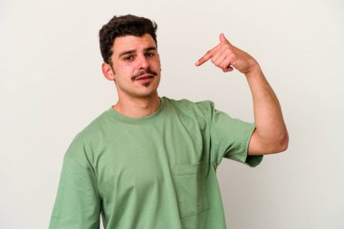 Beyaz arka planda yaşayan beyaz tenli genç bir adam gömlek fotokopi alanını gösteriyor, gururlu ve kendinden emin.