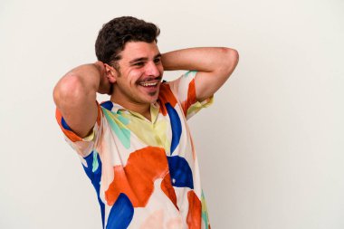 Beyaz arka planda izole olmuş genç beyaz bir adam kendini güvende hissediyor, elleri başının arkasında..