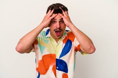 Beyaz arka planda izole edilmiş genç beyaz bir adam yüzünün yarısını palmiye ile örterek eğleniyor..