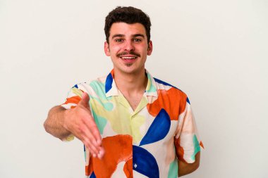 Beyaz arka planda izole edilmiş genç beyaz bir adam selamlama jesti olarak kameraya elini uzatıyor..