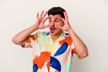 Beyaz arka planda izole edilmiş genç beyaz bir adam bir başarı fırsatı bulmak için gözlerini açık tutuyor..