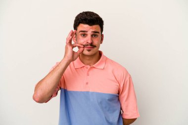 Beyaz arka planda izole edilmiş beyaz tenli genç bir adam parmakları dudaklarında bir sır saklıyor..