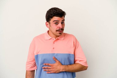 Beyaz arka planda izole edilmiş genç beyaz adam karnına dokunuyor, nazikçe gülümsüyor, yemek yiyor ve tatmin oluyor..