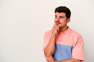 Beyaz arka planda izole edilmiş genç beyaz bir adam şüpheli ve şüpheci bir ifadeyle yana bakıyor..