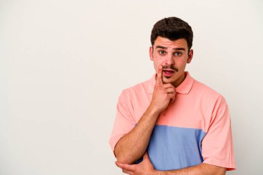 Beyaz arka planda izole edilmiş genç beyaz bir adam şüpheli ve şüpheci bir ifadeyle yana bakıyor..