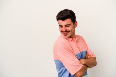 Beyaz arka planda izole edilmiş genç beyaz adam kollarını kavuşturarak gülümsüyor..