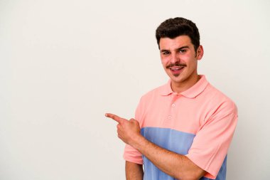 Beyaz arka planda izole edilmiş genç beyaz bir adam gülümsüyor ve boş alanda bir şeyler gösteriyor..