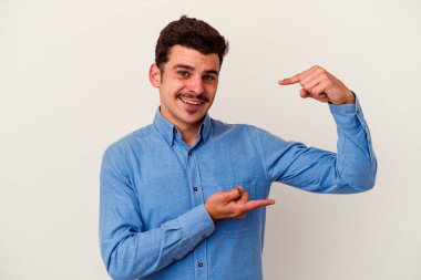 Beyaz arka planda izole edilmiş genç beyaz bir adam işaret parmaklarıyla küçük bir şey tutuyor, gülümsüyor ve kendinden emin..