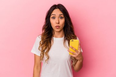 Pembe arka planda izole edilmiş cep telefonu tutan genç Meksikalı kadın omuzlarını silker ve gözleri açık kalır..