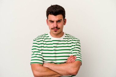 Beyaz arka planda izole edilmiş, hoşnutsuzca kaşlarını çatmış, kollarını kavuşturmuş genç beyaz bir adam..