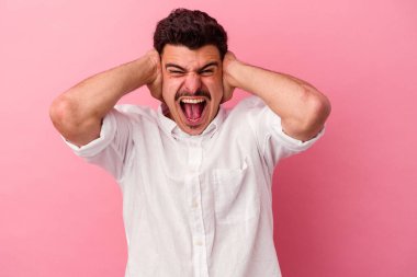 Kafkasyalı genç adam pembe arka planda izole edilmiş kulakları kulaklarıyla kapatıyor çok fazla ses duymamaya çalışıyor..