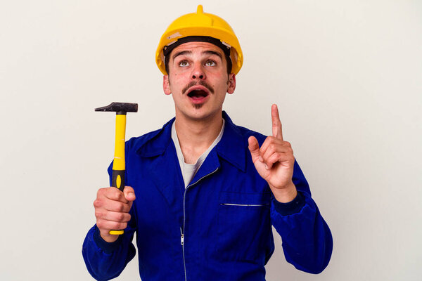 Young caucasian worker man holding a hammer isolated on white background pointing upside with opened mouth.