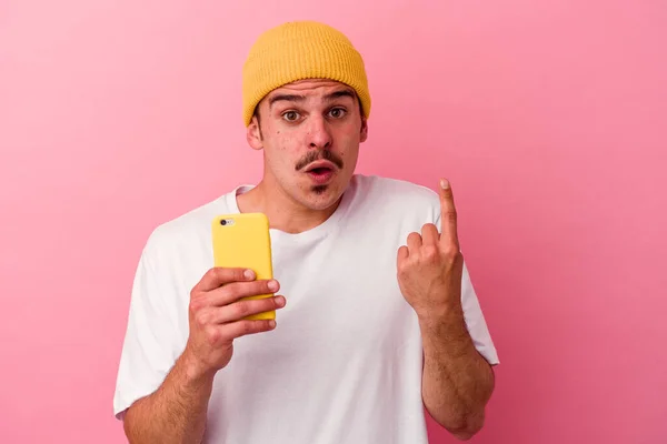 Młody Biały Mężczyzna Trzymając Telefon Komórkowy Różowym Tle Mając Jakiś — Zdjęcie stockowe