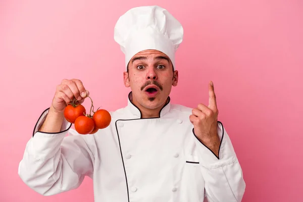 年轻的高加索厨师 手持被粉色背景隔离的西红柿 有一些伟大的想法 创意的概念 — 图库照片