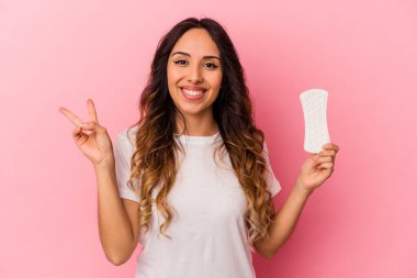 Pembe arka planda izole edilmiş bir kompres tutan genç Meksikalı kadın neşeli ve kaygısız parmaklarıyla barış sembolü gösteriyor..