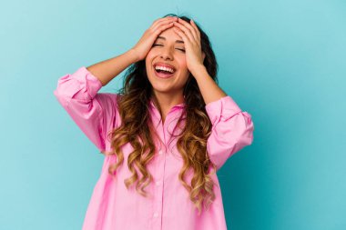 Mavi arka planda izole edilmiş genç Meksikalı kadın mutlu bir şekilde ellerini başının üstünde tutuyor. Mutluluk kavramı.