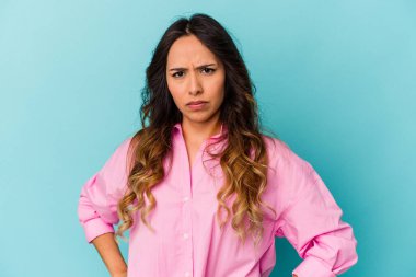 Mavi arka planda izole edilmiş genç Meksikalı kadın hoşnutsuzca kaşlarını çatmış, kollarını kavuşturmuş..