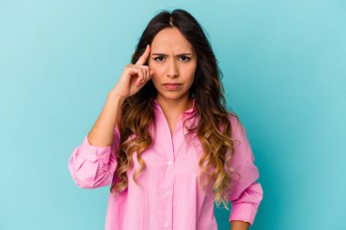 Mavi arka planda izole edilmiş genç Meksikalı kadın şakağı parmağıyla işaret ediyor, düşünüyor ve bir göreve odaklanıyor..