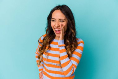 Mavi arka planda izole edilmiş genç Meksikalı kadın heyecanlı bir şekilde bağırıyor..