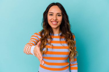 Mavi arka planda izole edilmiş genç Meksikalı kadın selamlama jesti olarak kameraya elini uzatıyor..