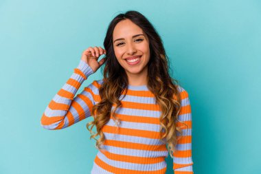 Mavi arka planda izole edilmiş genç Meksikalı bir kadın bir şeye gülüyor, elleriyle ağzını kapatıyor..