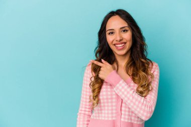 Mavi arka planda izole edilmiş genç Meksikalı kadın gülümsüyor ve boş alanda bir şeyler gösteriyor..