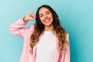 Mavi arka planda izole edilmiş genç Meksikalı kadın zaferi, tutkuyu ve coşkuyu kutluyor, mutlu bir ifade..