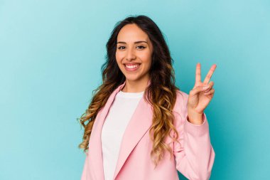 Mavi arka planda izole edilmiş genç Meksikalı kadın neşeli ve tasasız parmakları olan bir barış sembolü gösteriyor..
