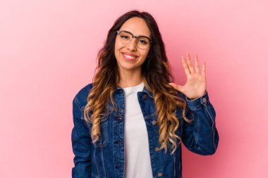 Pembe arka planda izole edilmiş genç Meksikalı kadın gülümseyerek beş numarayı parmaklarıyla gösteriyor..