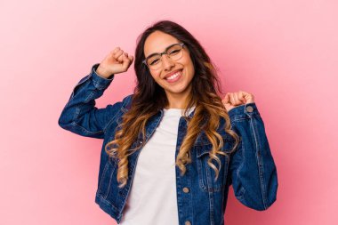 Pembe arka planda izole edilmiş genç Meksikalı kadın özel bir günü kutluyor, atlıyor ve enerjiyle kollarını kaldırıyor..