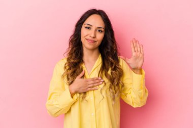 Pembe arka planda izole edilmiş genç Meksikalı kadın yemin ediyor, elini göğsüne koyuyor..