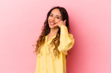 Pembe arka planda izole edilmiş genç Meksikalı kadın parmakları olan bir cep telefonu hareketi gösteriyor..