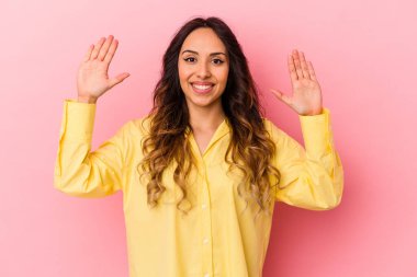 Pembe arka planda izole edilmiş genç Meksikalı kadın hoş bir sürprizle karşılaşıyor, heyecanlı ve el kaldırıyor..