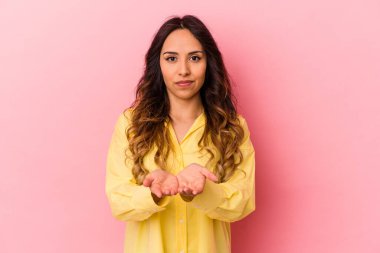 Pembe arka planda izole edilmiş genç Meksikalı kadın elinde avuç içi bir şeyle kameraya sunuyor..
