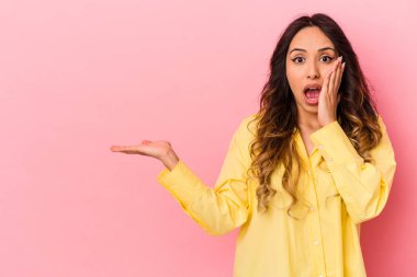 Pembe arka planda izole edilmiş genç Meksikalı kadın avuç içi fotokopi alanı tutmaktan etkilenmiş..